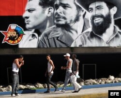 Un grupo de jóvenes camina frente a un cartel alusivo a la Unión de Jóvenes Comunistas (UJC).